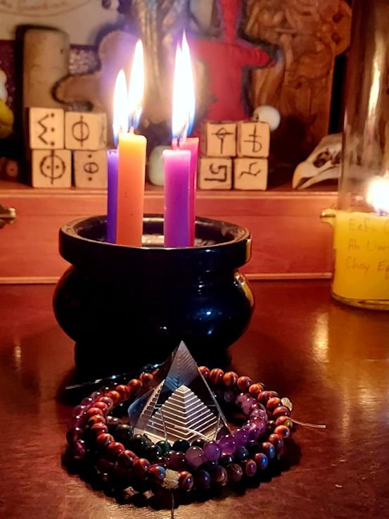 4 candles burning in a cauldron with a small glass pyramid in front